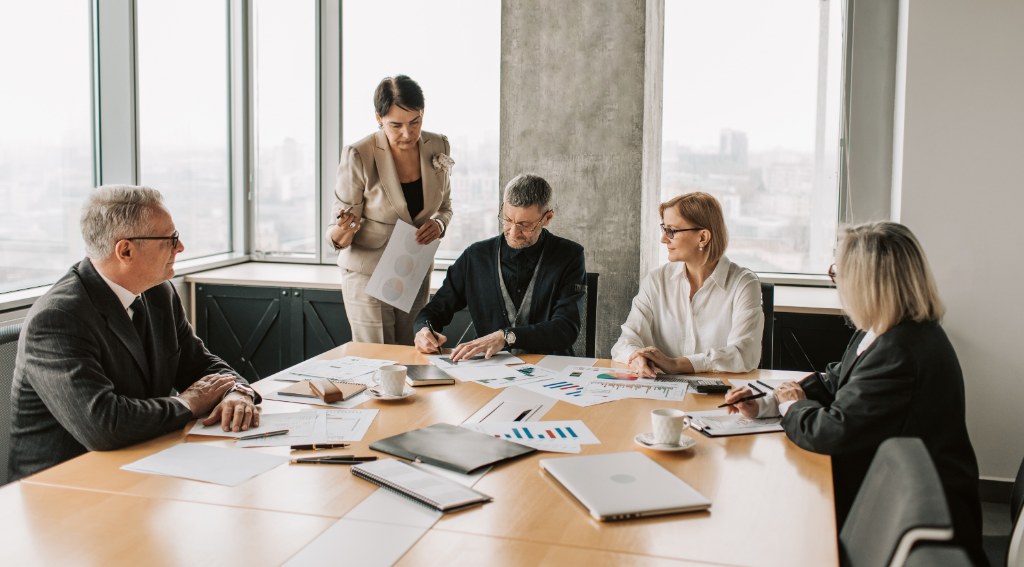 LLC vs. S-Corp vs. Sole Proprietor — how liability, tax and payroll differ Five business colleagues reviewing printed financial charts and documents around a boardroom table in a high-rise office