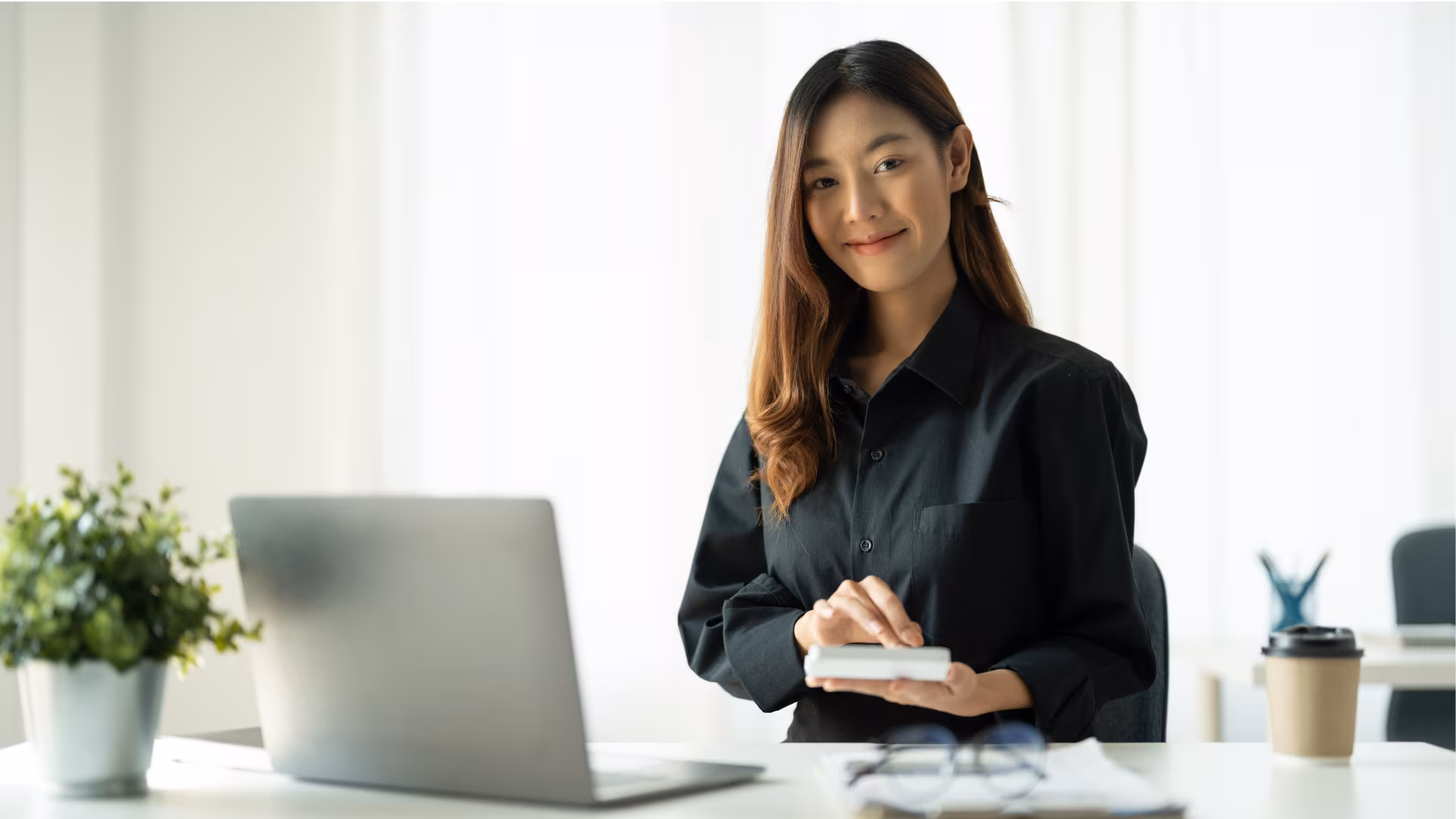 1099 Threshold 2026 — the new $2,000 rule and how to issue a 1099 Smiling businesswoman in a black shirt working a calculator at a bright office desk with a laptop